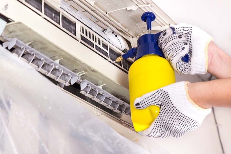Blog Title: AC Maintenance Checklist Photo: Technician cleaning wall hanging AC unit